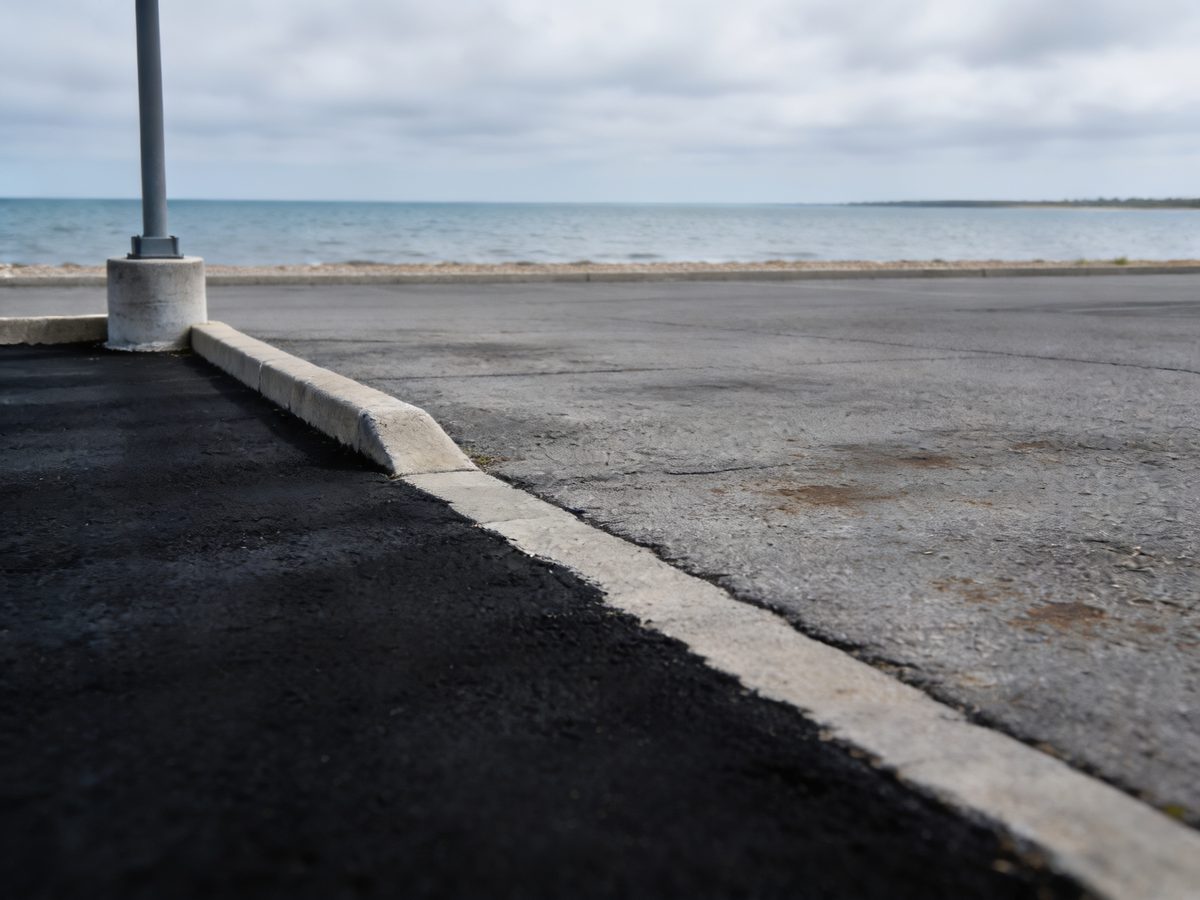 A lakeside parking lot with a freshly sealcoated section beside faded grey asphalt